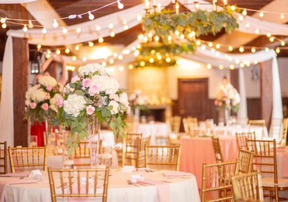 Beautiful wedding reception with greenery and draped fabric on ceiling with tall vases of white hydrangea and pink roses on each wedding reception table. Pink and white wedding florals.