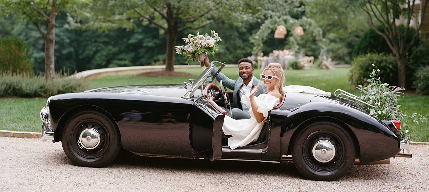 mixed race bride and groom in vintage black sports car, summer styled wedding at Bramblewood