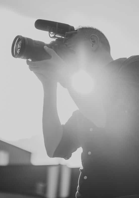 Black & white photo of Brian Schornberg holding camera. Schornberg Wedding Films