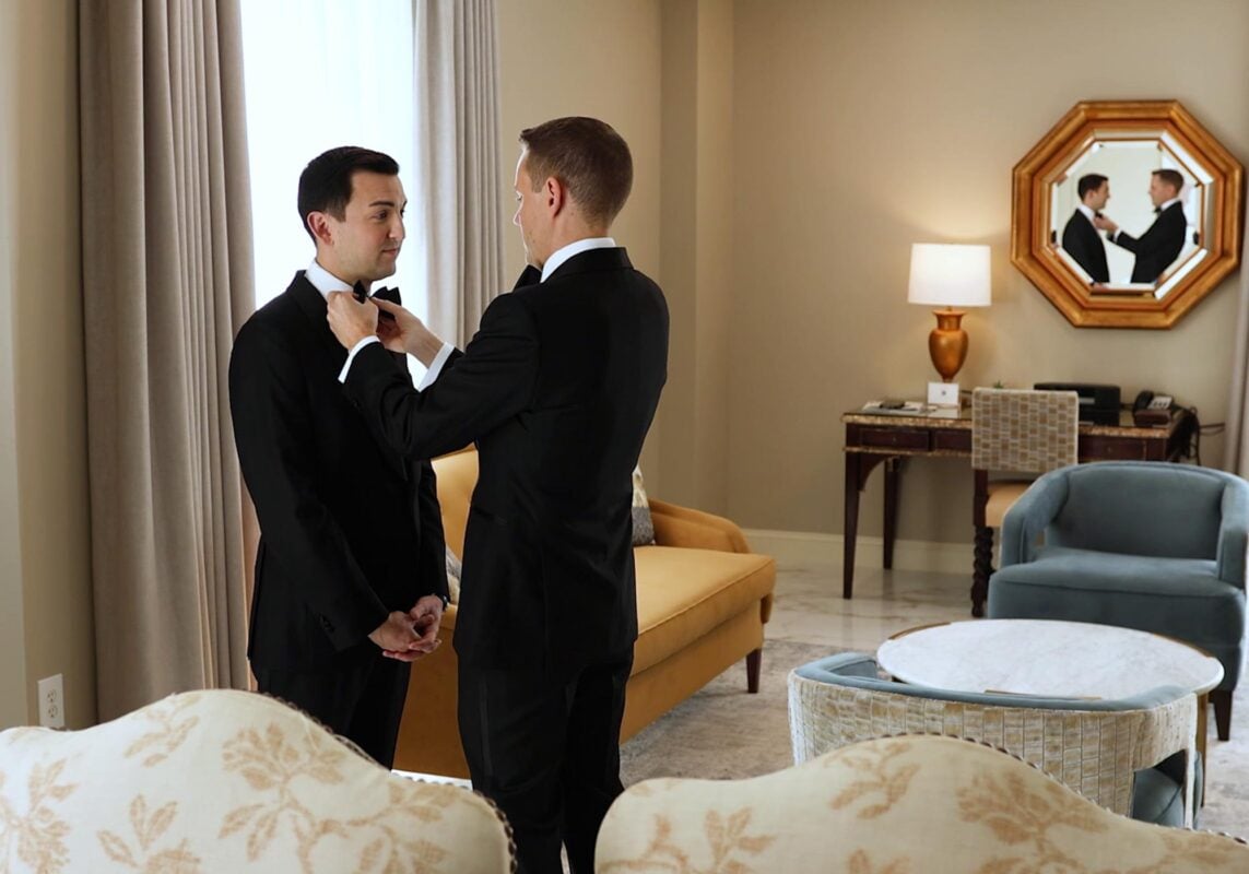 Groomsman helping groom to get ready by doing his bowtie. Schornberg Wedding Films